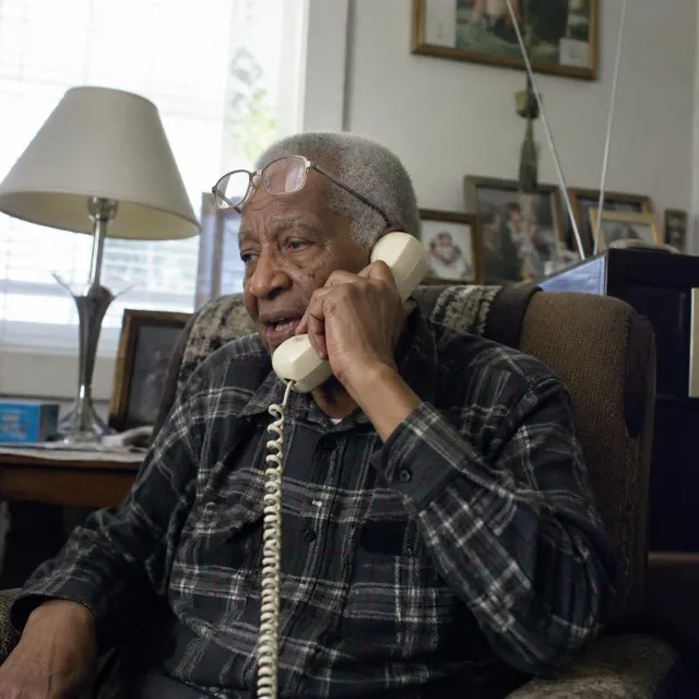 An older man talking on a landline phone in his living room